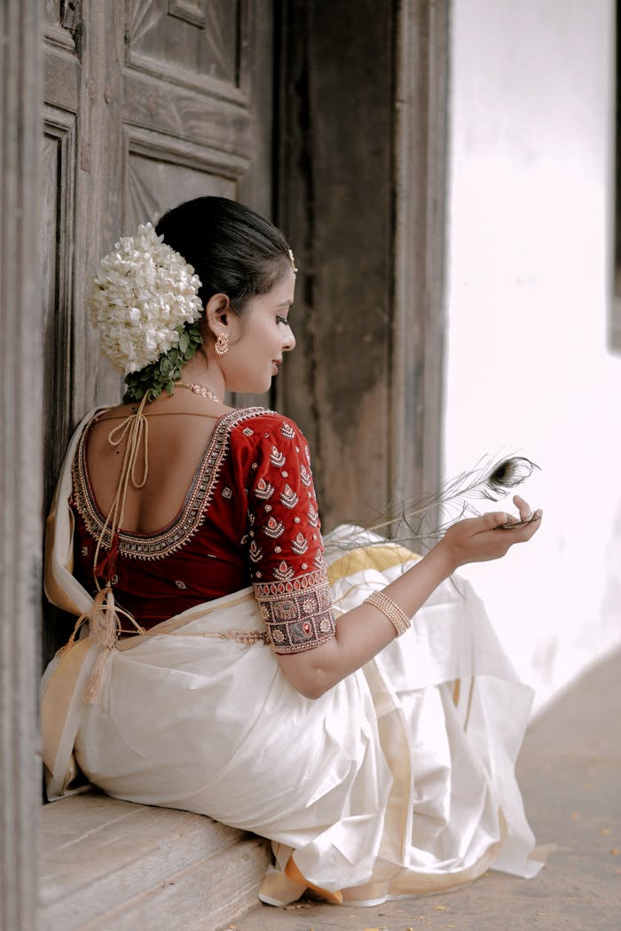 A woman in Indian traditional dress holding peacock feather, sitting gracefully.