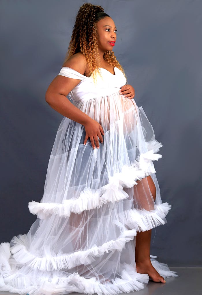 Portrait of a pregnant woman in a sheer white gown, exuding elegance and grace.