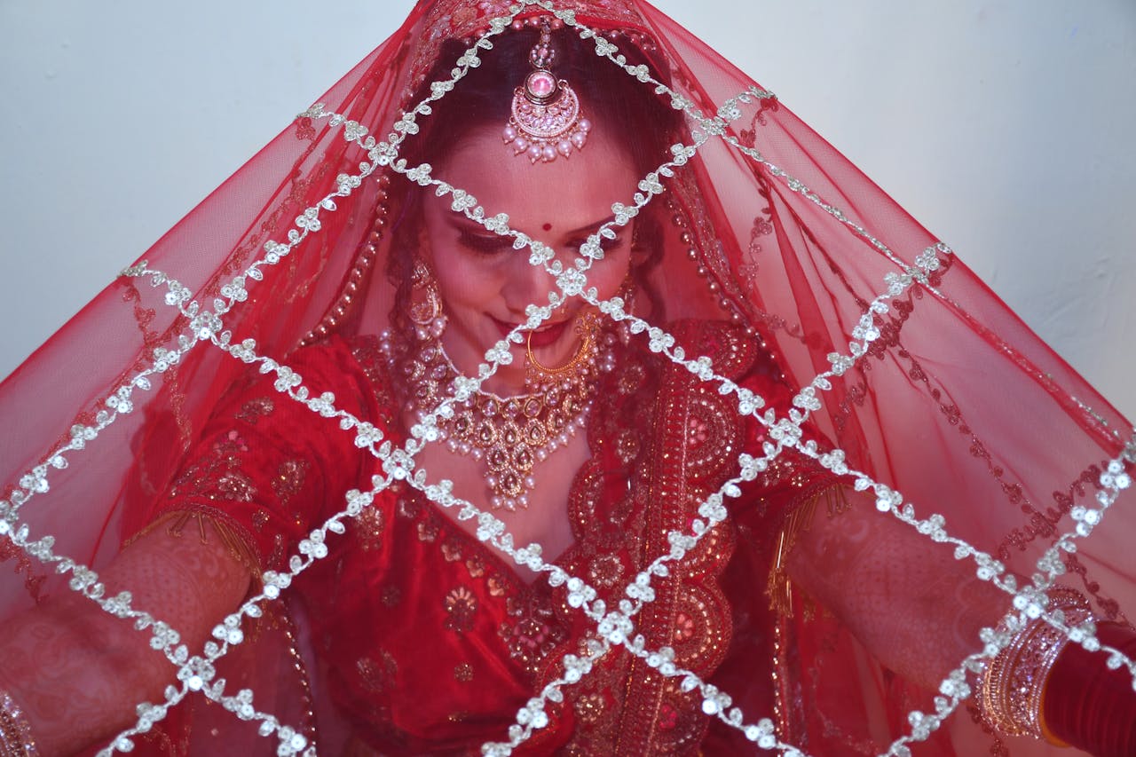 A stunning Indian bride adorned in gold jewelry beneath a red veil, exemplifying cultural elegance.