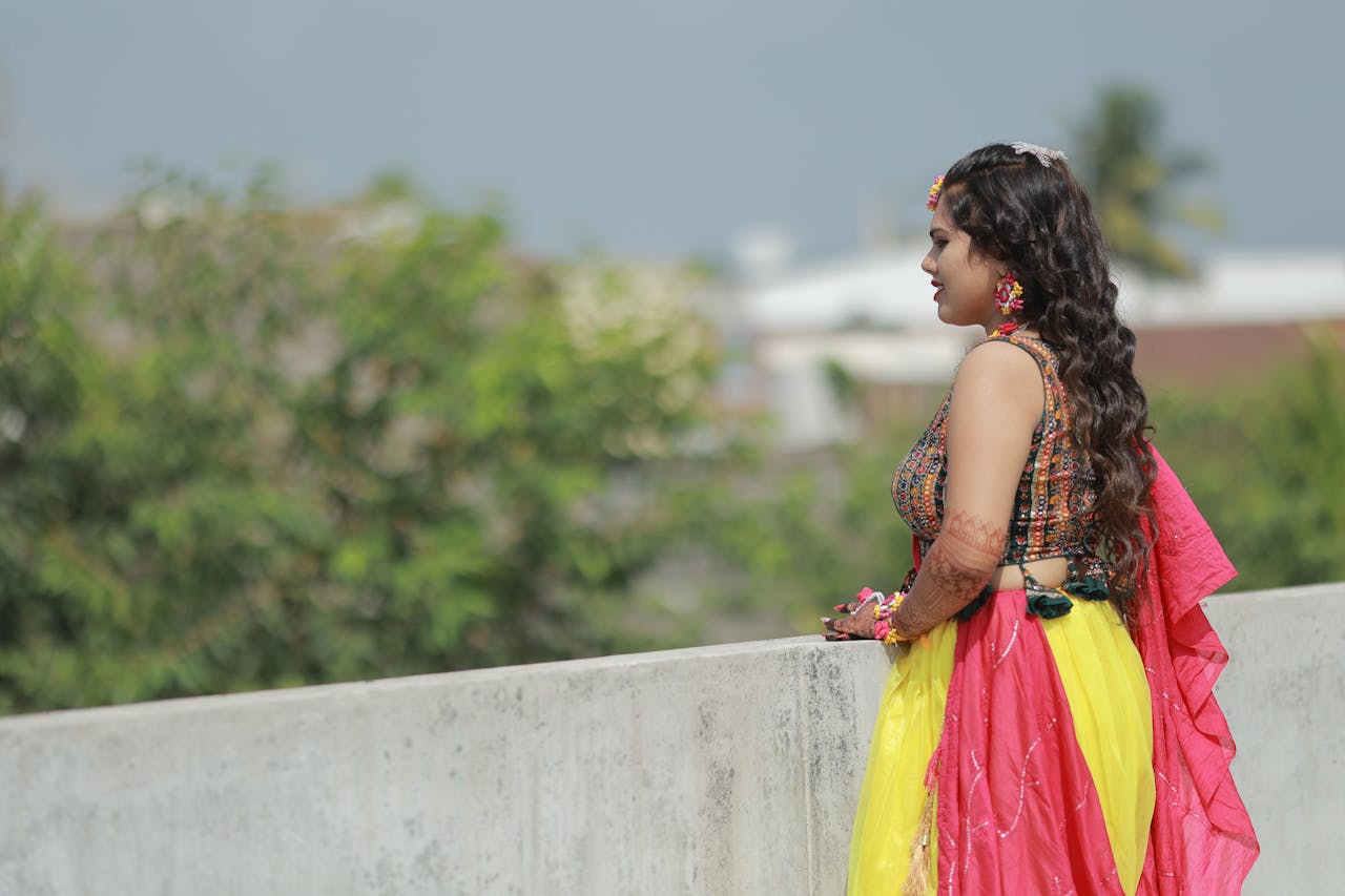 A vibrant portrait of an Indian bride in traditional attire with henna, posing outdoors.